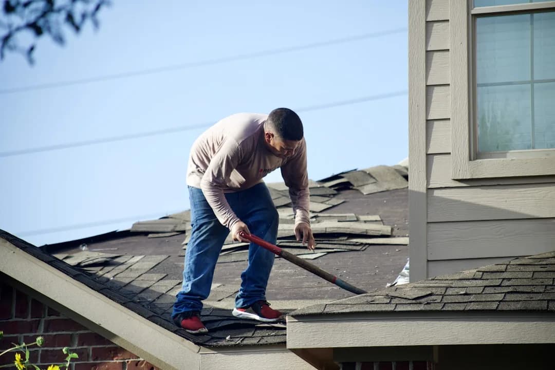 A roofer strips old shingles off a residential roof during a tear-off before a new install.