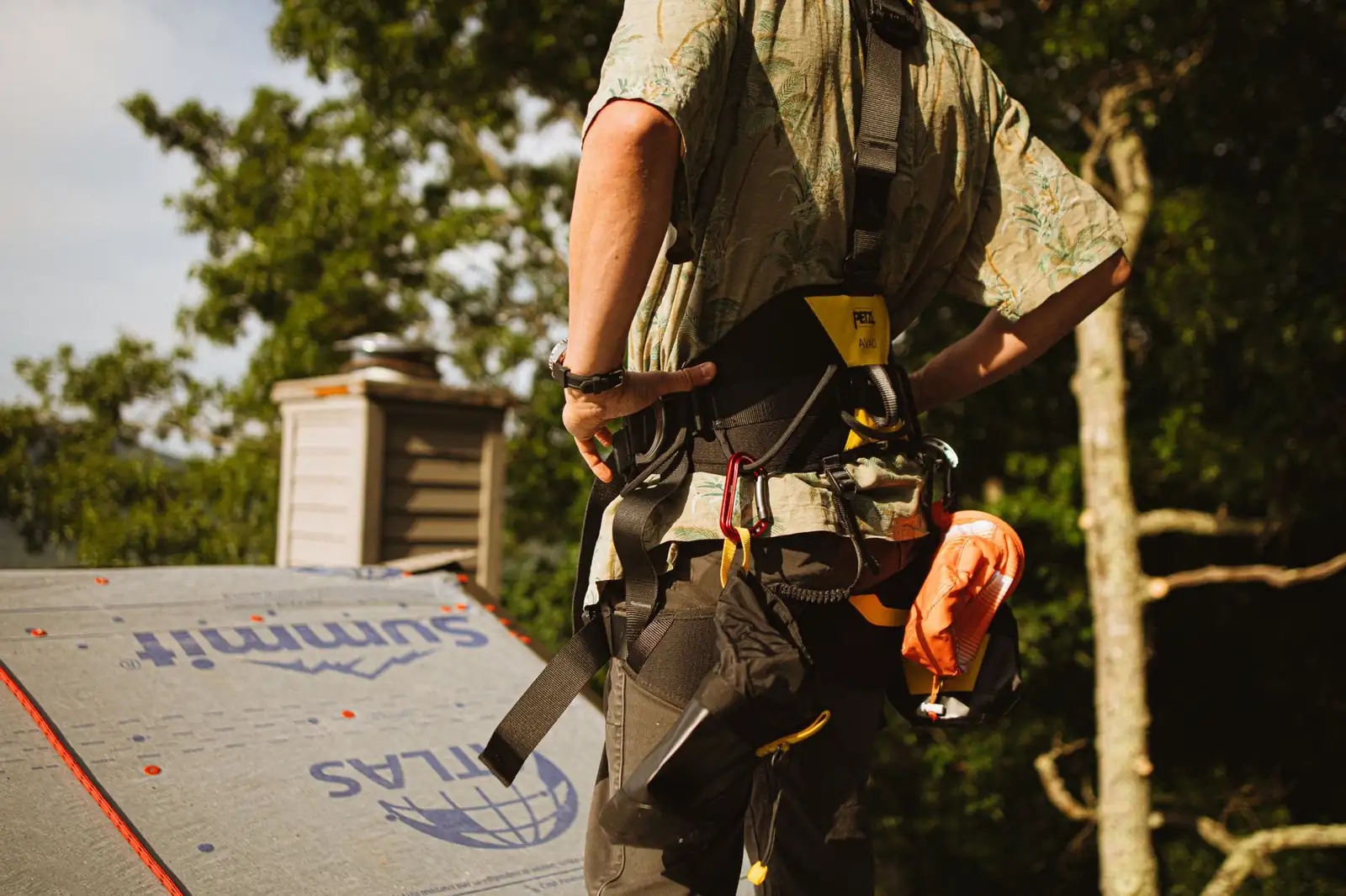 Roofer in a safety harness working on a steep residential rooftop.