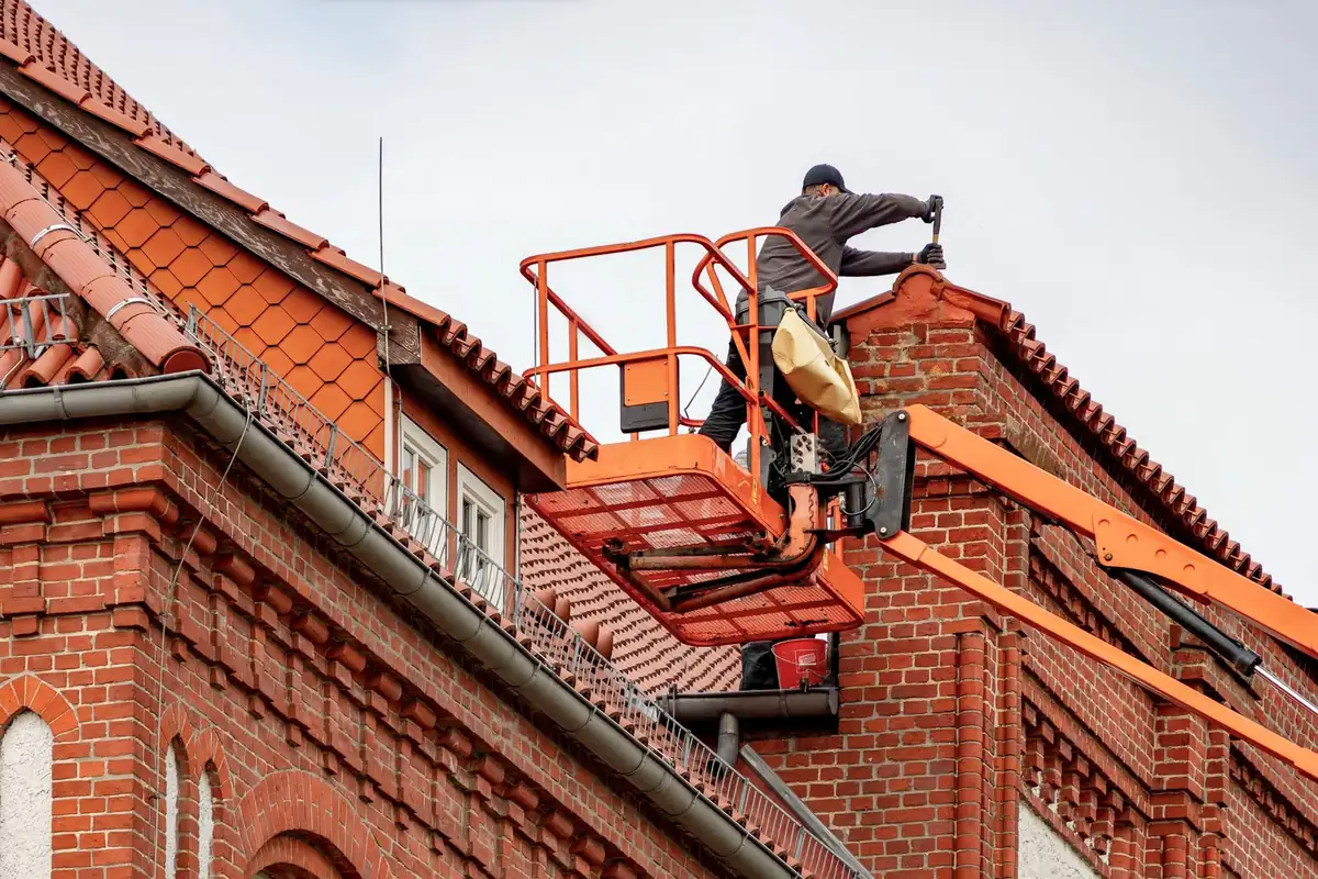 A roofer in a cherry picker doing maintenance on a residential roof